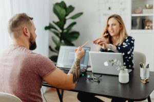 Man and woman discussing work at a table with laptops in a modern office.