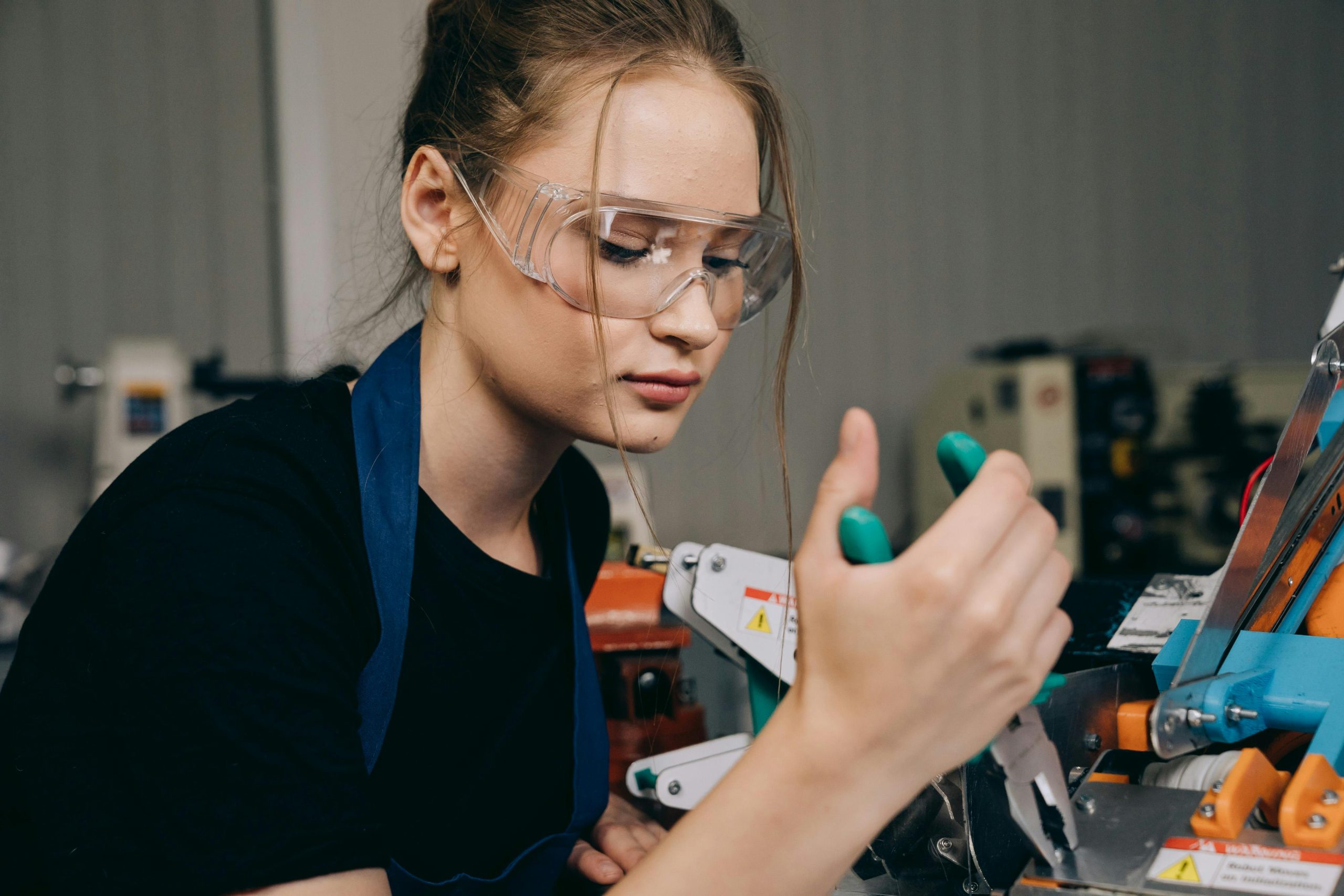 Focused female engineer using pliers in a workshop setting while wearing protective goggles.